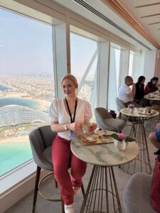 Joelle Monroe vor einem Panoramafenster mit der Skyline von Dubai im Hintergrund.